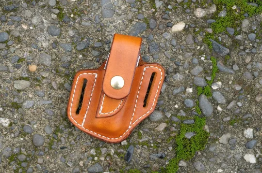 Front view of a Leatherman Charge multitool sheath shown in saddle tan leather with a brass snap