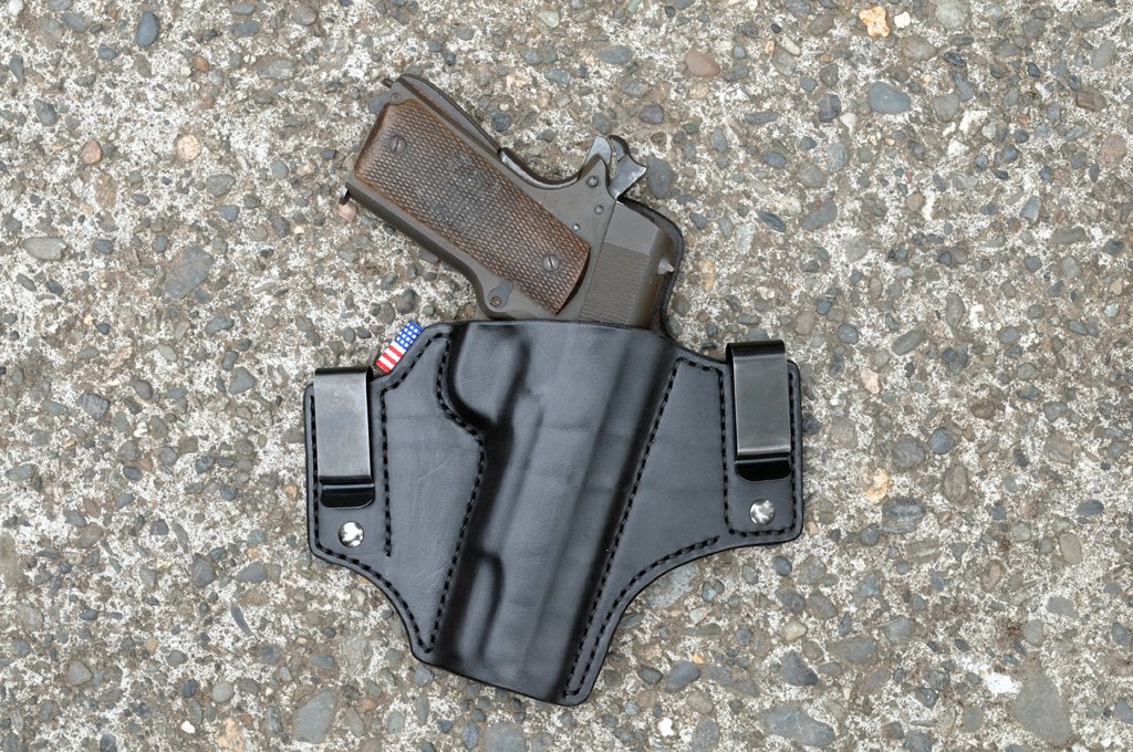Front view of a black leather inside waistband holster for a 1911 pistol sitting on a cement surface