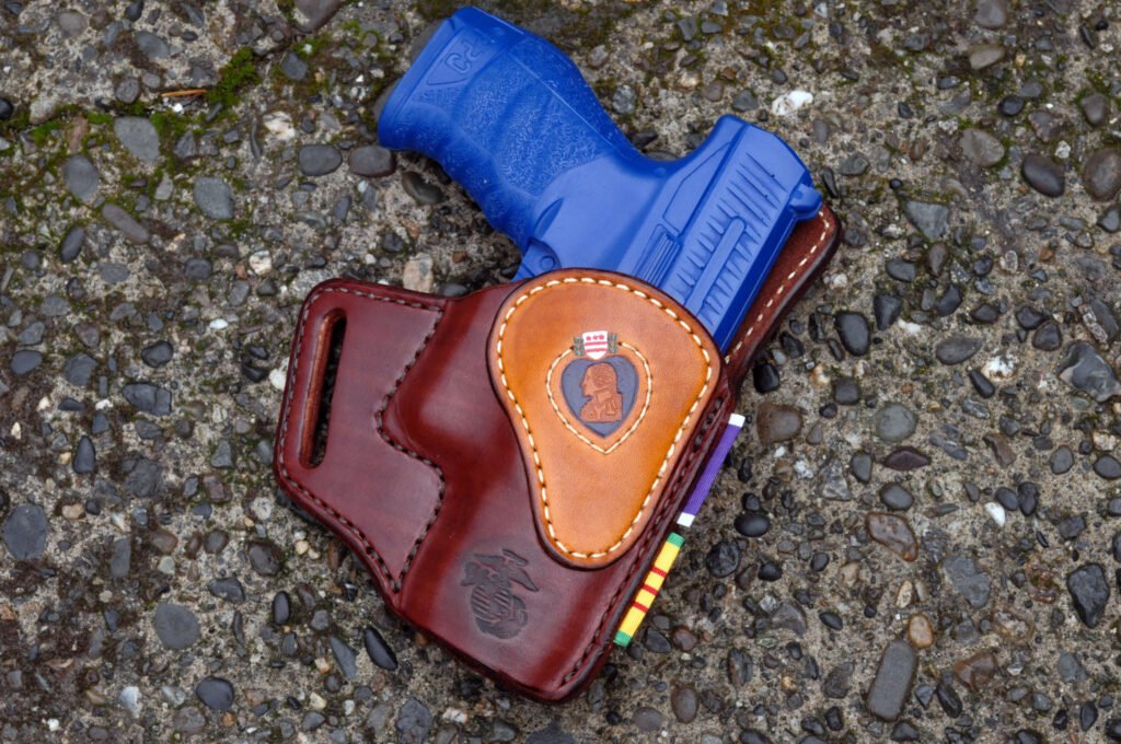 Front view of a holster for a Walther PPQ pistol. The holster is of mahogany dyed leather with a trim piece of saddle tan leather on the front. It has a stamped design of a purple heart medal and the US Marine Corps Eagle Globe and Anchor emblem stamped on it.