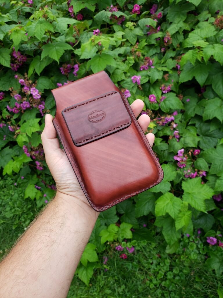 Back view of a leather holster for two phones held in front of green vegetation.