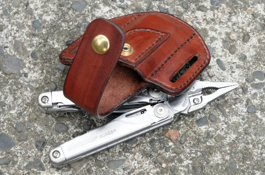 Artistic view of a Leatherman Surge multitool sheath shown in mahogany leather with a brass snap