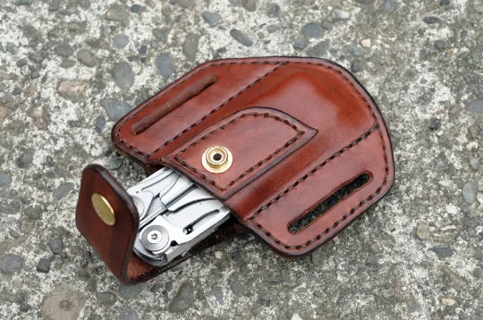 Artistic view of a Leatherman Surge multitool sheath shown in mahogany leather with a brass snap