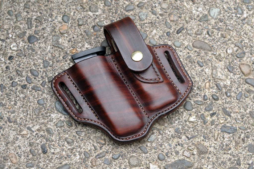 Front view of a chocolate brown holster for a Leatherman Signal and a pistol magazine sitting on a cement surface