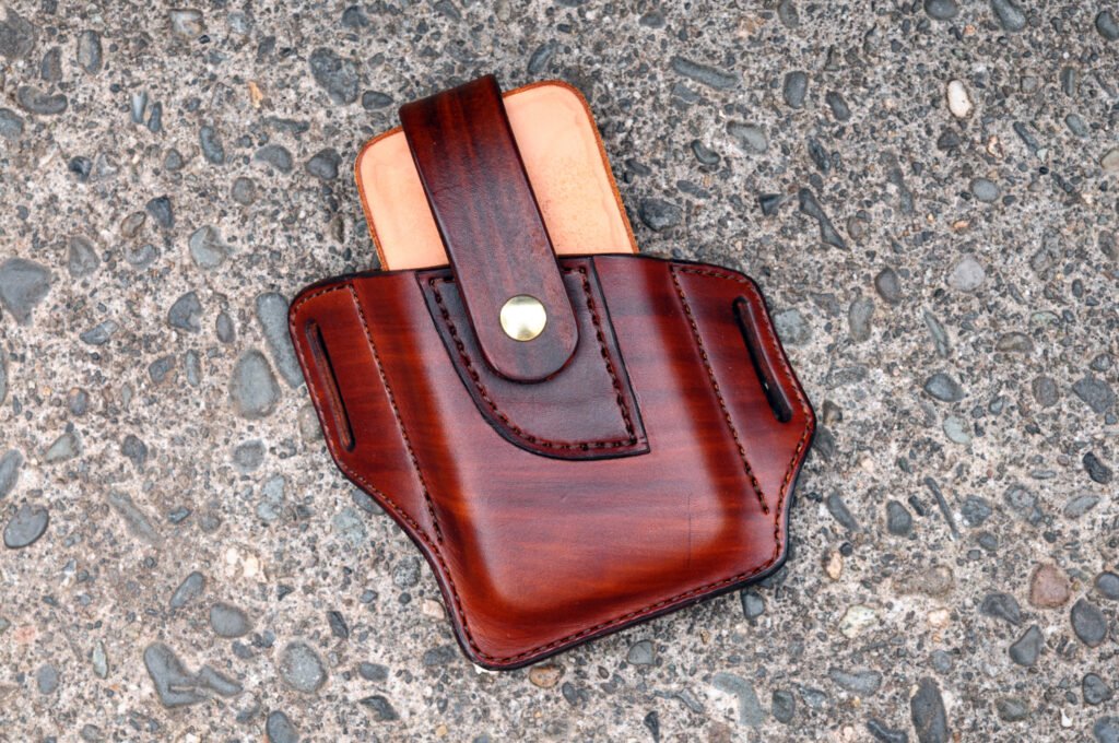 Front view of a leather phone holster with a snap down retention strap over the top.
