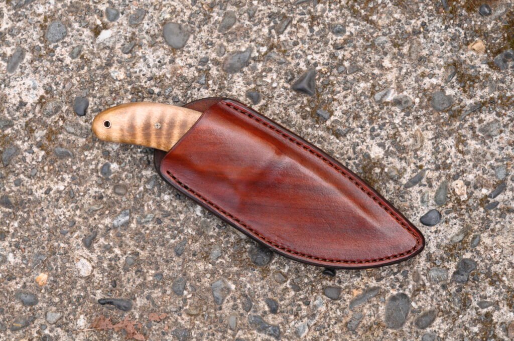 Front view of a custom brown leather knife sheath sitting on a cement surface