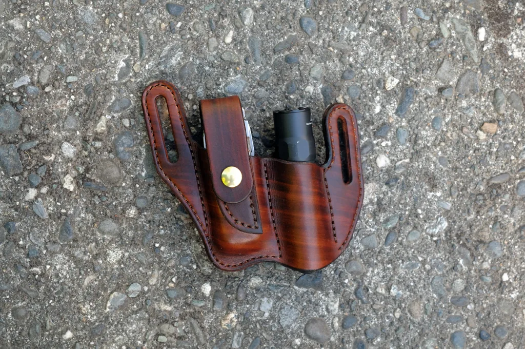 Front view of a brown leather sheath for a Leatherman Surge and Surefire flashlight sitting on a cement surface