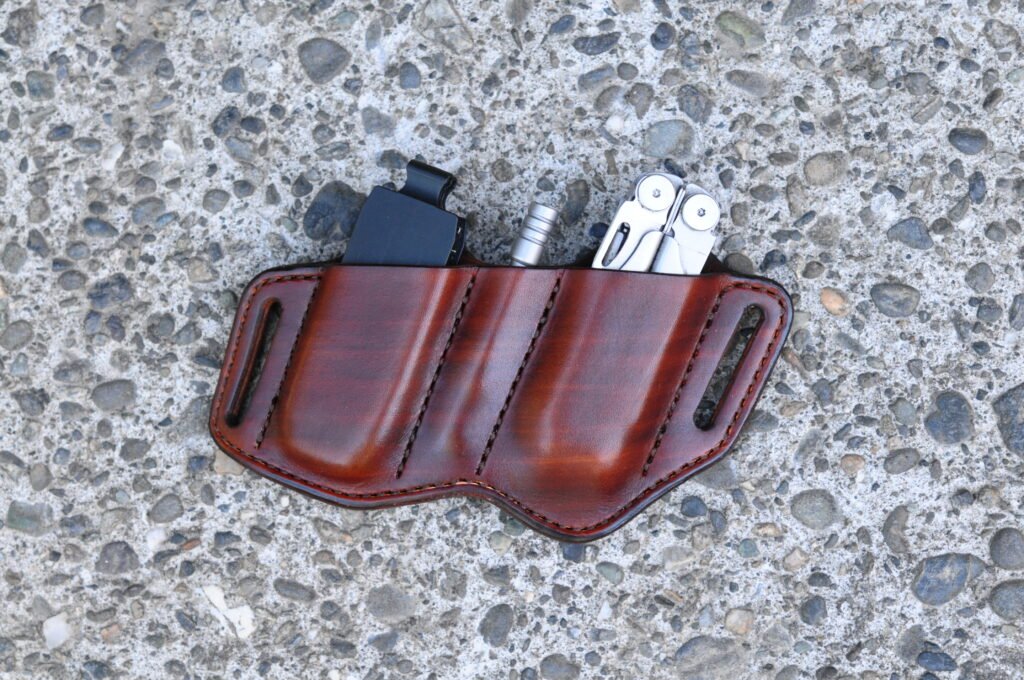 Front view of a brown leather open top sheath for a Leatherman Surge multitool and the driver bit and extension set sitting on a cement surface.