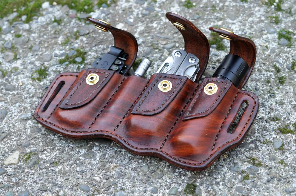 Artistic photo of a holster for a Leatherman Charge with driver bit set and extension and a Surefire E1B flashlight sitting on a mossy cement surface