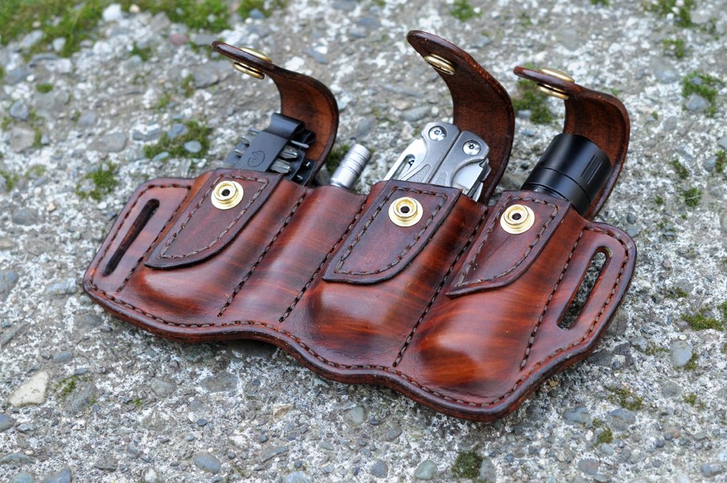 Artistic photo of a holster for a Leatherman Charge with driver bit set and extension and a Surefire E1B flashlight sitting on a mossy cement surface