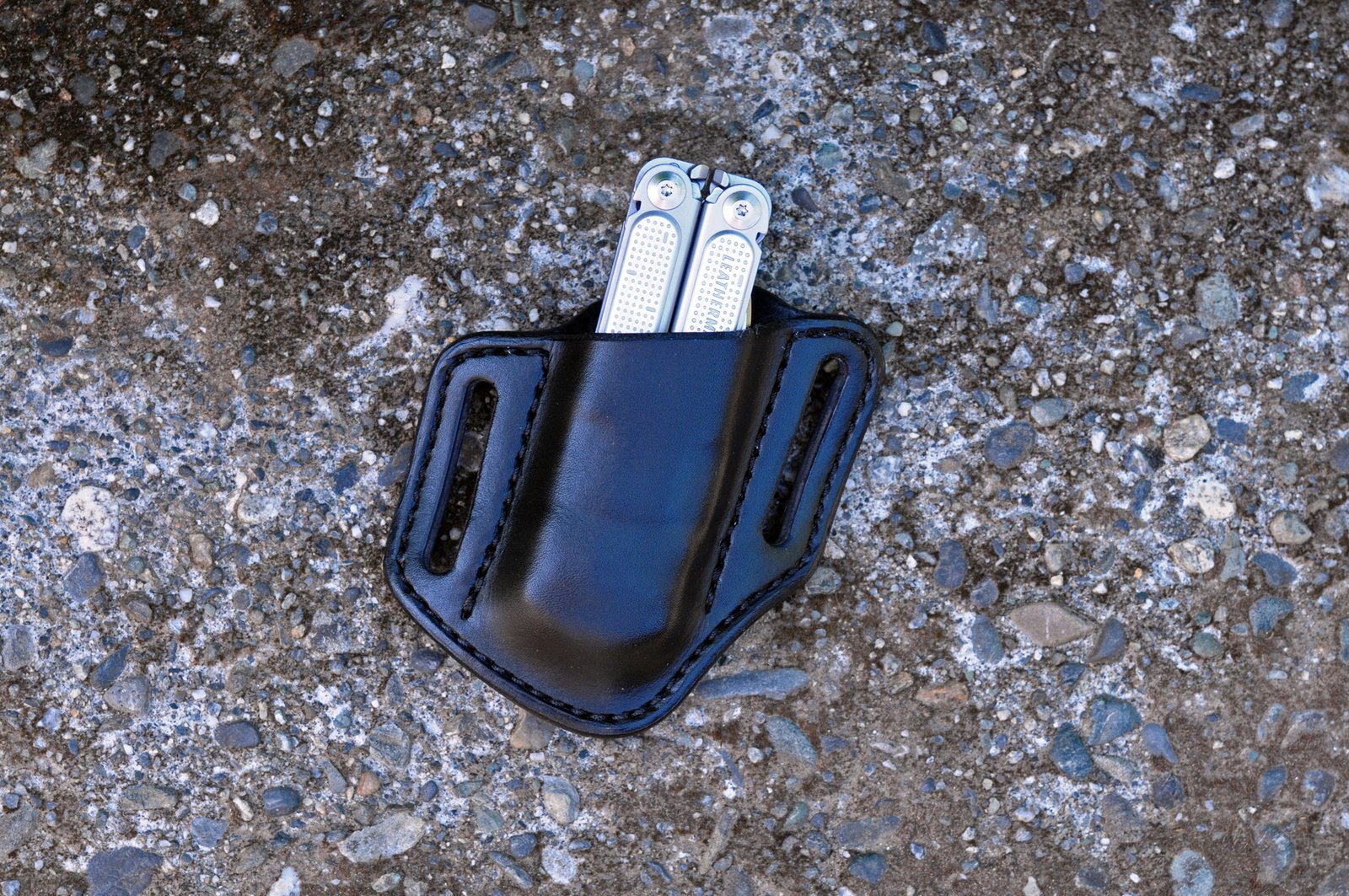 Front view of a black leather open top Leatherman Free P4 holster sitting on a cement surface