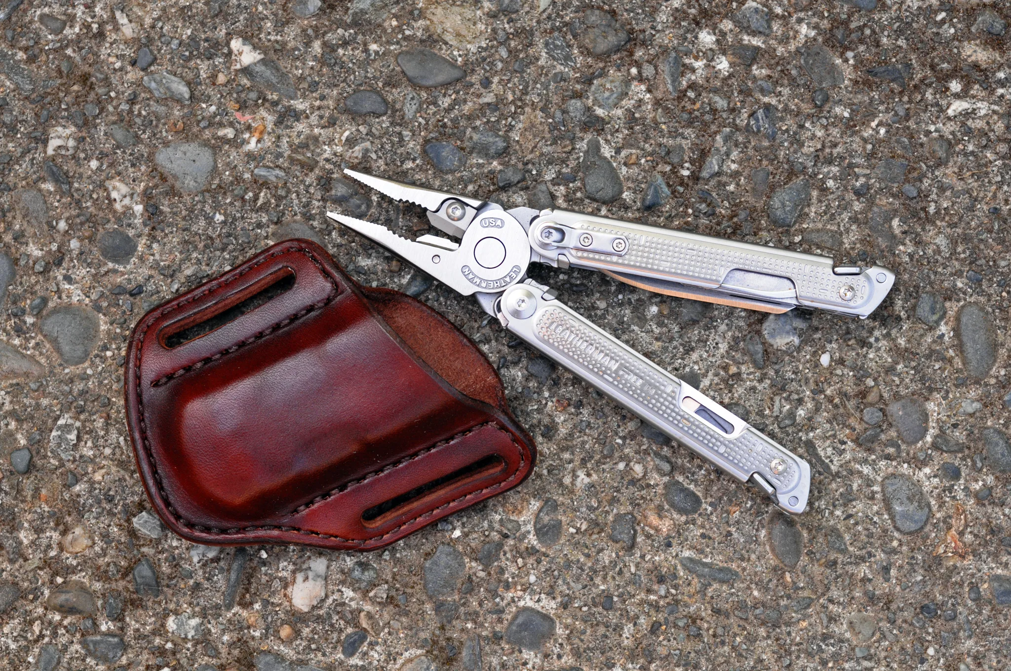 Artistic view of a mahogany leather open top sheath and Leatherman Free P4 multitool sitting on a cement surface