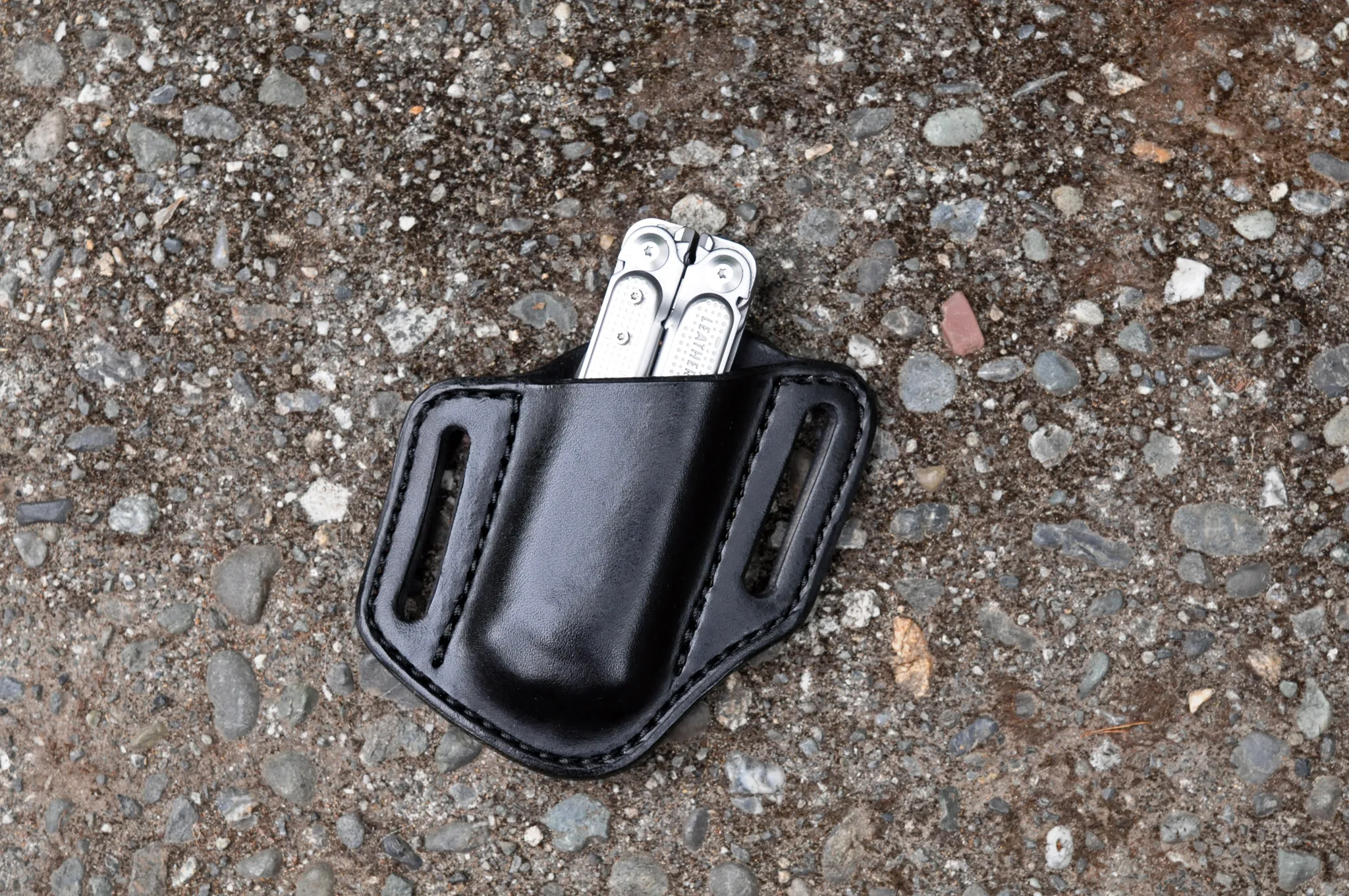 Front view of a black leather open top sheath for a Leatherman Free P4 multitool sitting on a cement surface.