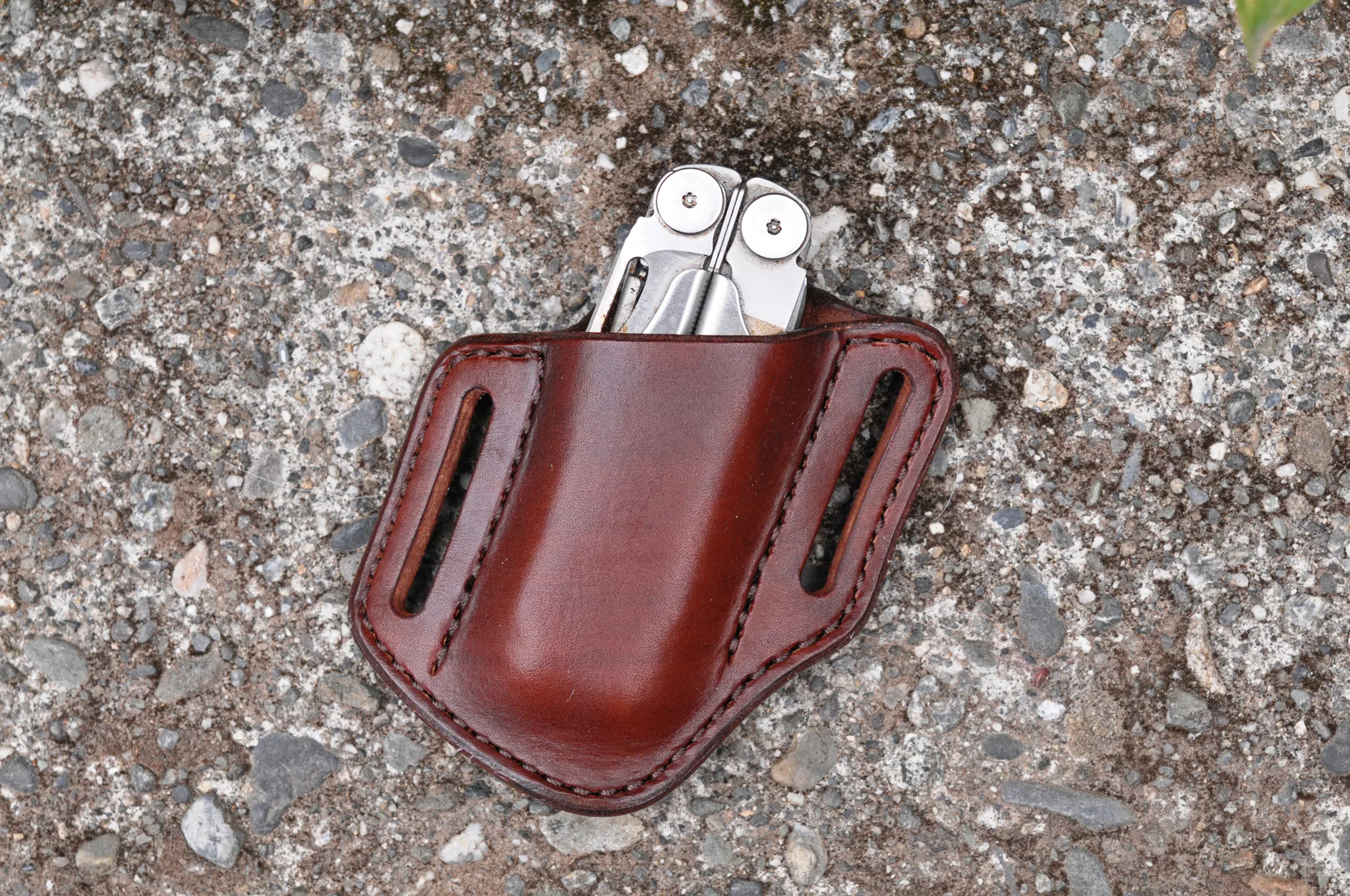 Front view of a sheath for a Leatherman Wave multitool handmade from Mahogany dyed leather. It's sitting on a cement surface
