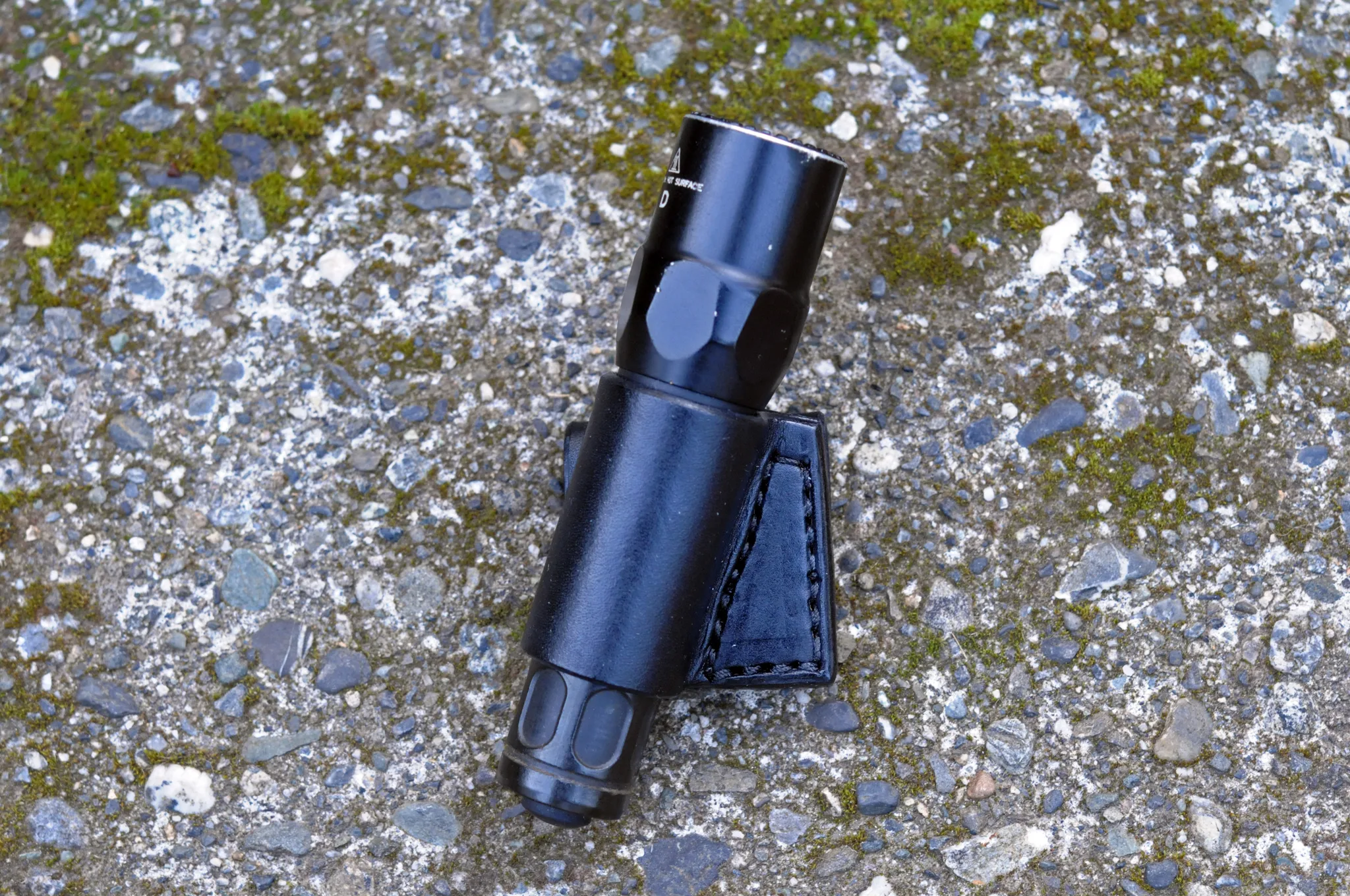 Front view of a black leather flashlight belt holster sitting on a mossy cement surface