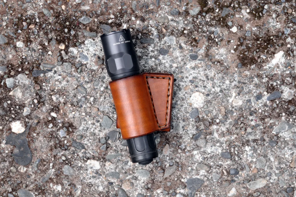 Front view of a light brown leather flashlight belt holster sitting on a cement surface